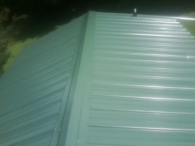 New green metal panels meeting at the ridge of a roof — Flat Roof Repair work by our crew in Tupelo