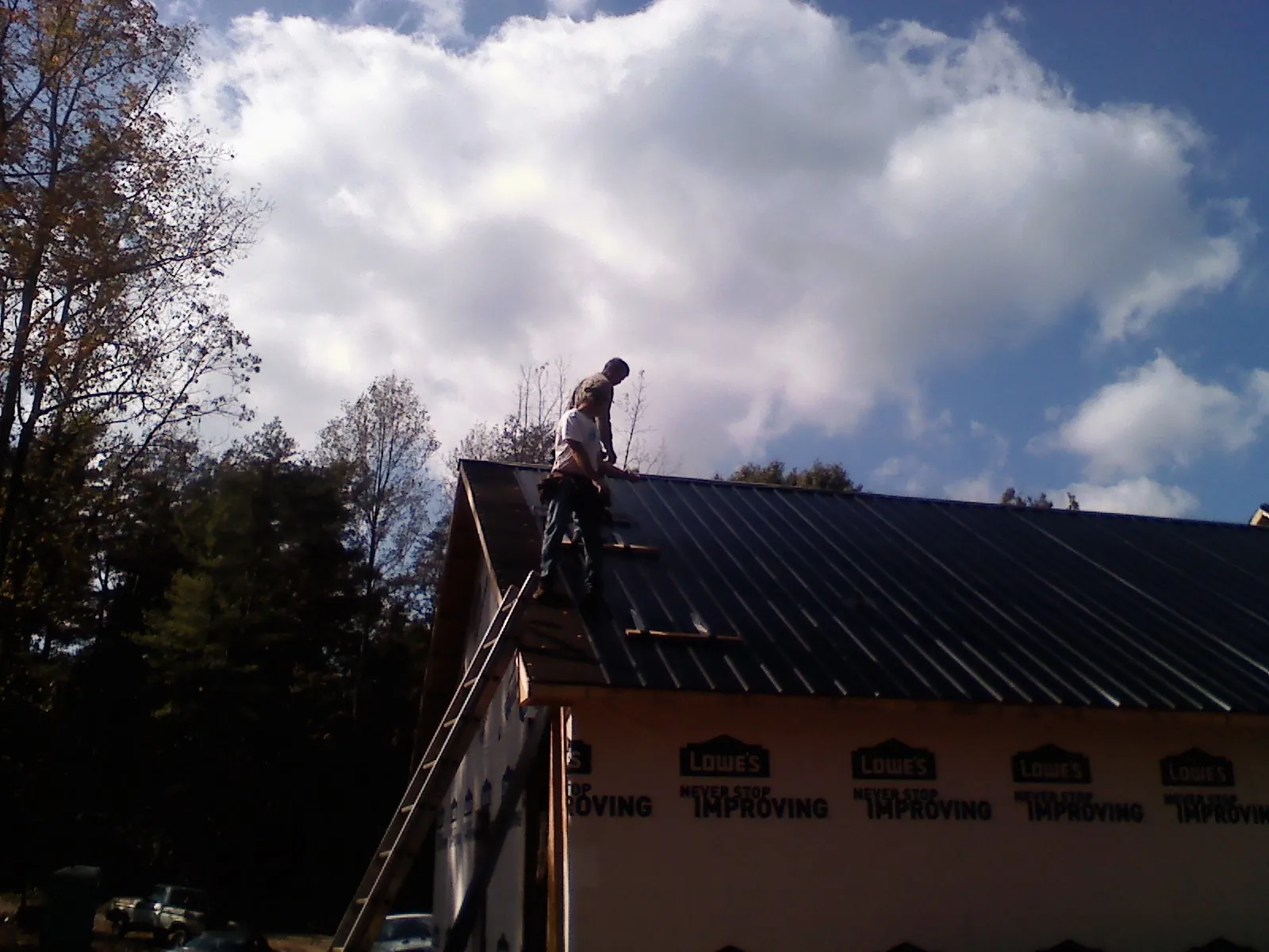 Roofer fastening dark metal panels high against a cloudy sky, from a Roof Inspection job in Tupelo