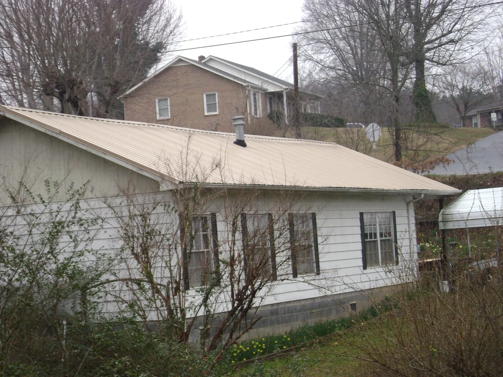 Tan metal roof on a white sided house set into a hillside — Commercial Roofing by Roofing Brothers in Tupelo